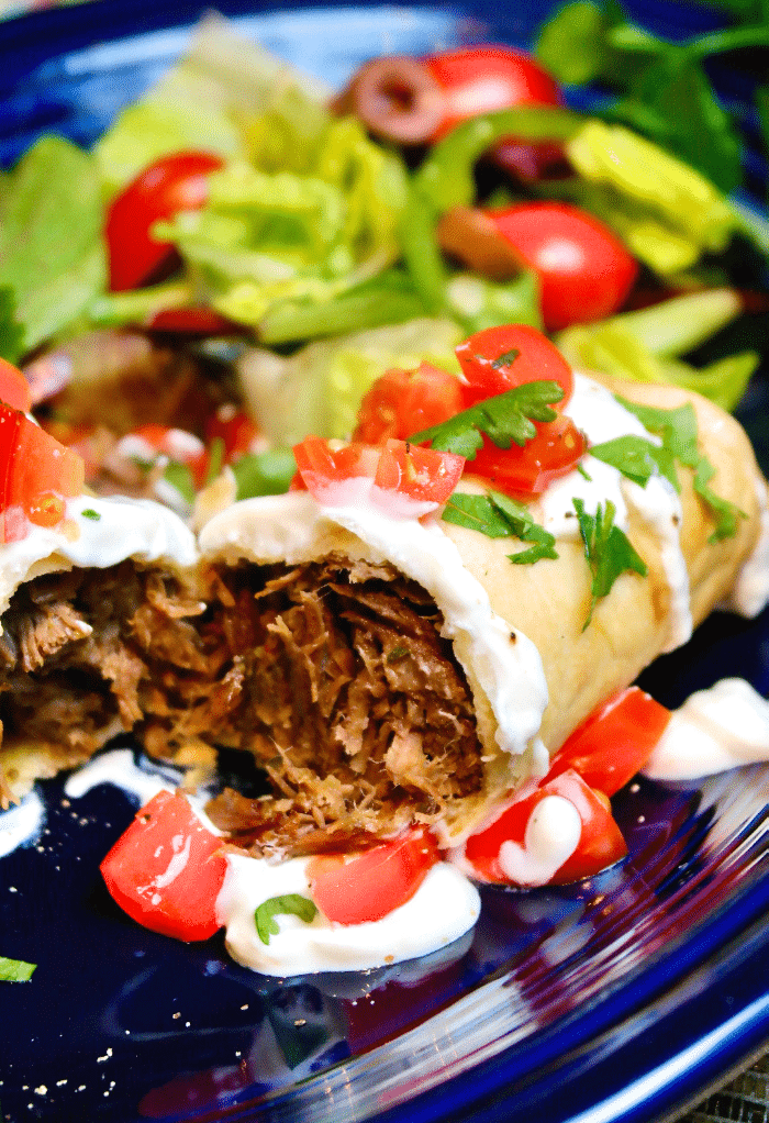 Beef chimichanga cut in half and topped with tomatoes and sour cream.