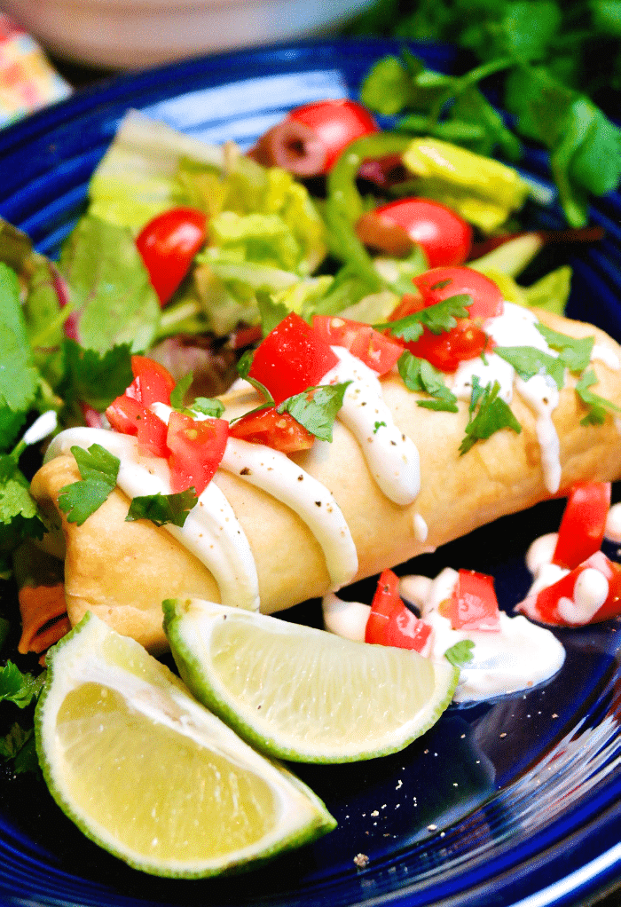 Shredded Beef Chimichanga on a blue plate topped with sour cream and tomatoes. 