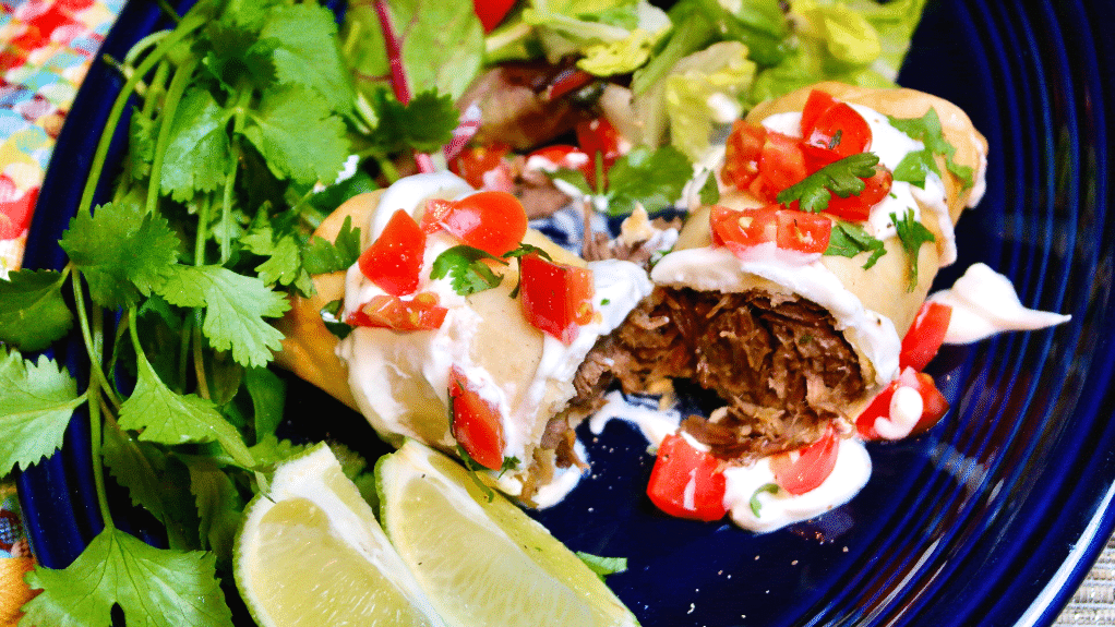 Top view of a cooked beef chimichanga topped with tomatoes and cilantro. 