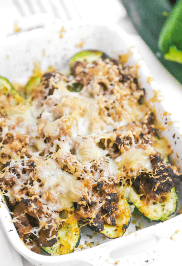 Air fryer zucchini stuffed with hamburger and topped with cheese in a white casserole dish.