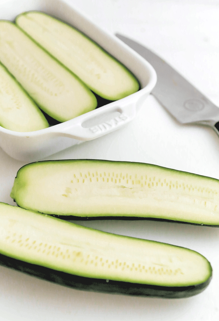 Zucchini sliced in half and some placed in a white baking dish.