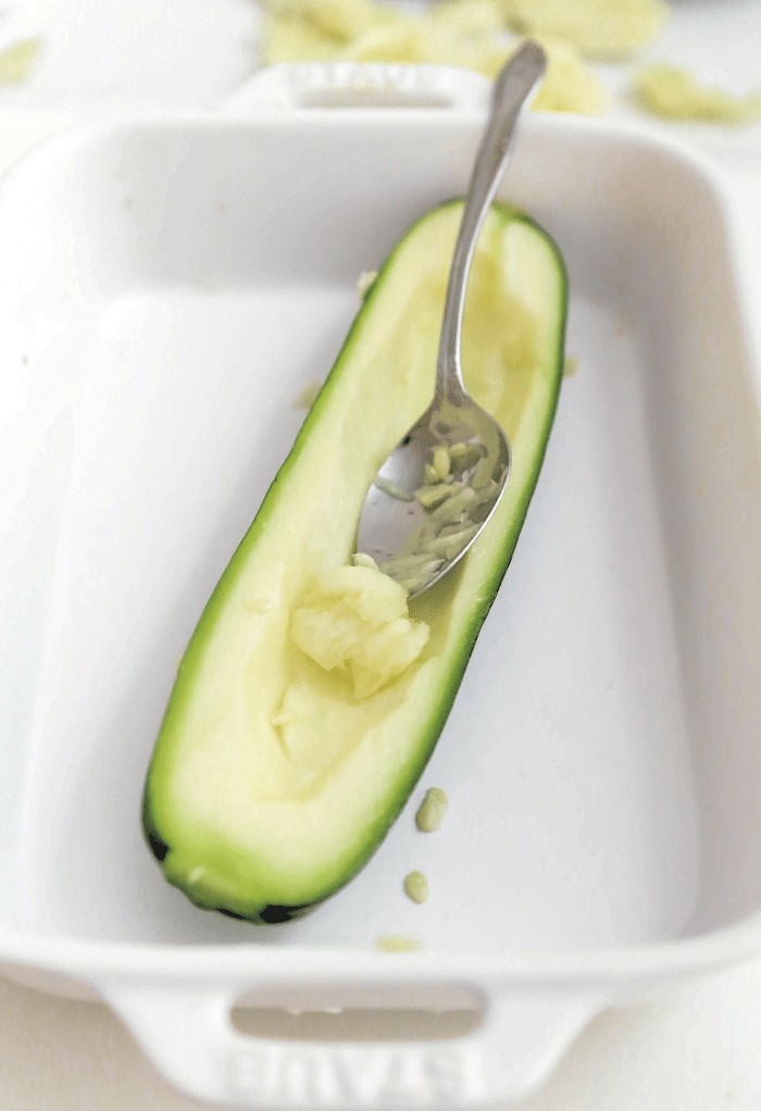 Scooping out the seeds of a zucchini getting ready to fill it with hamburger.