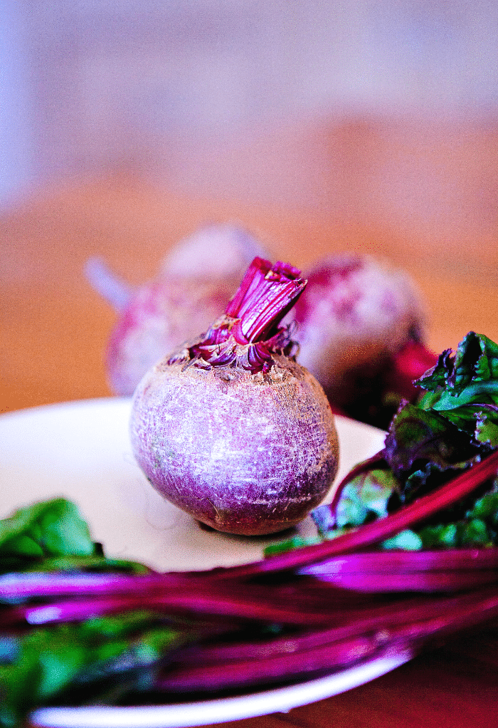 One raw beet on a white plate with the green tops. 