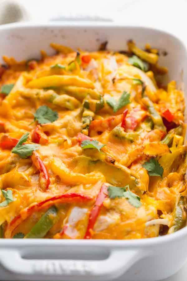 Closeup view of red and green bell peppers with melted cheese and chicken in a white baking dish