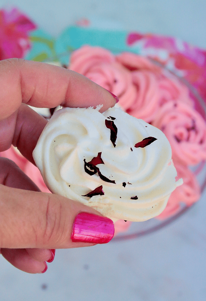 A hand with pink painted nails holding a white meringue cookie.