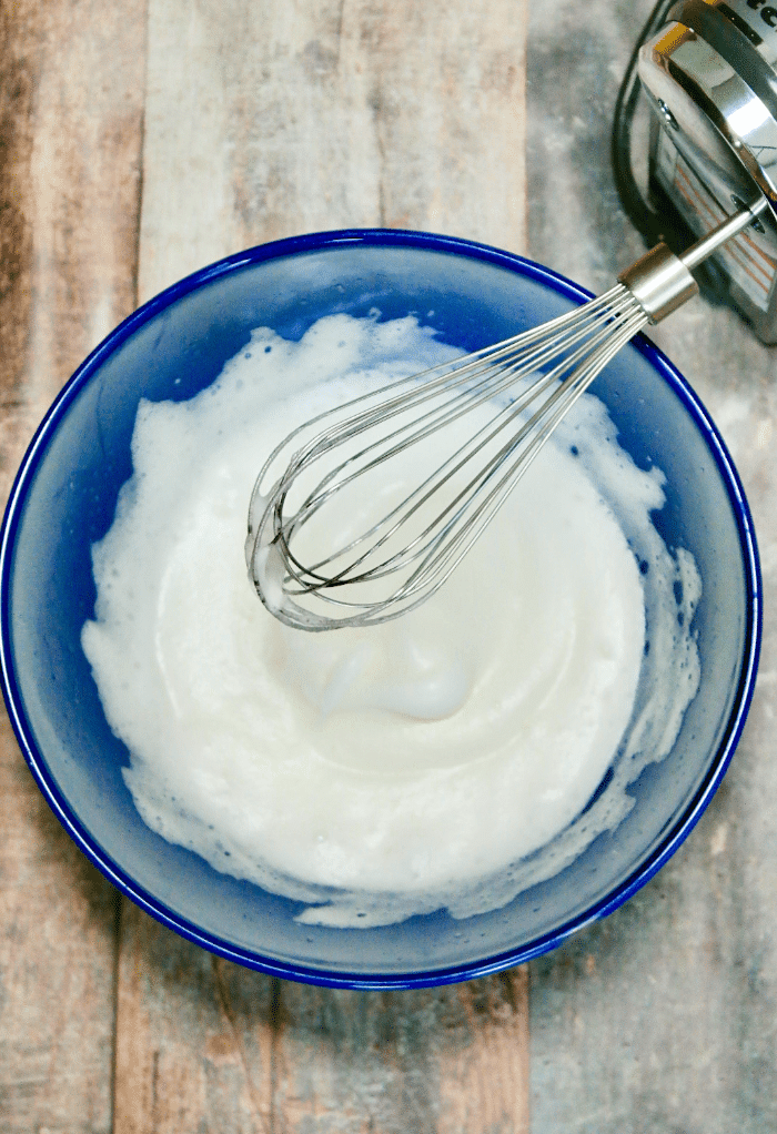 Foamy egg whites in a blue mixing bowl. 