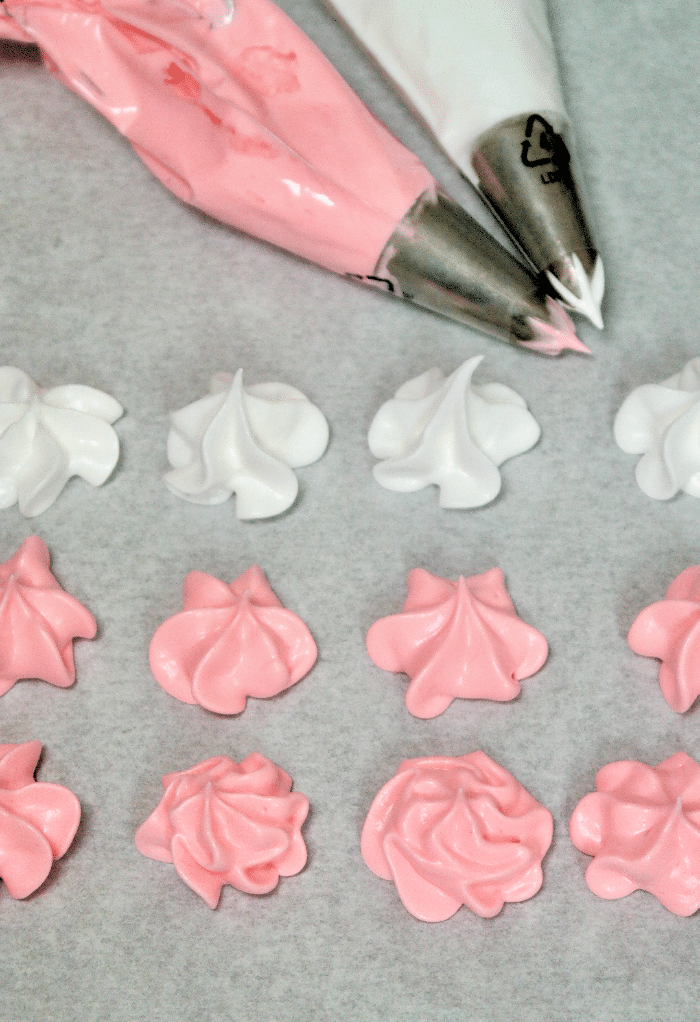 Pink and white meringue kisses before baking with piping bags on the side. 