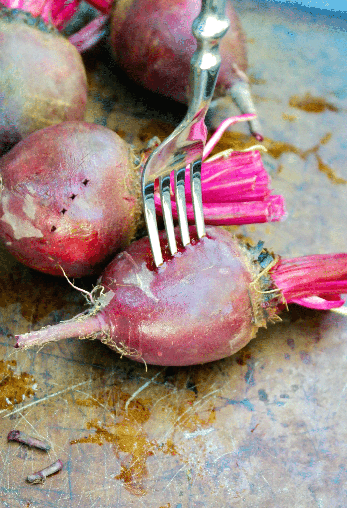 Piercing a raw beet with a fork before roasting.