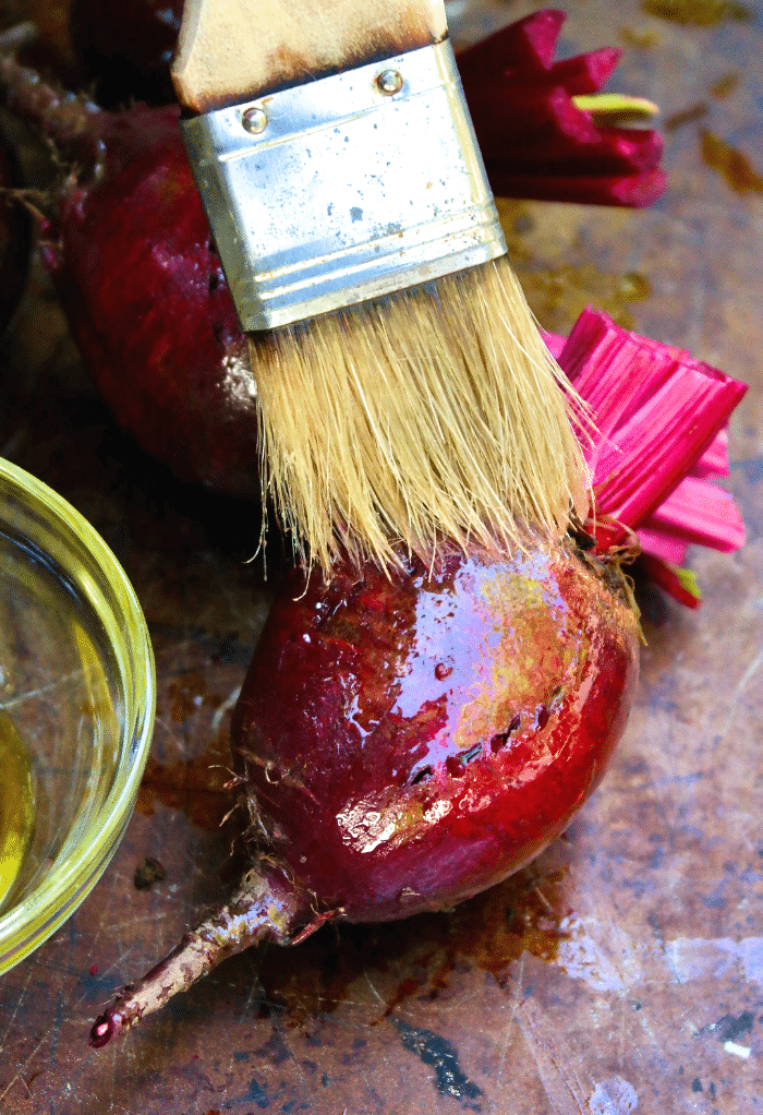 Brushing a raw beet with olive oil before roasting.