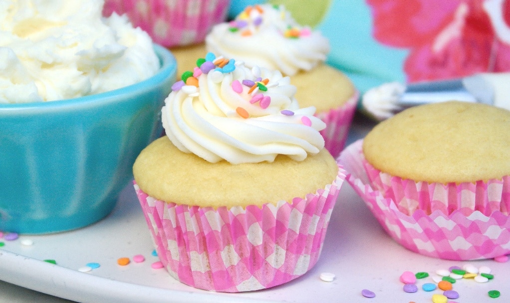 Sugar free vanilla cupcakes on a platter with a small teal bowl on the side filled with vanilla buttercream frosting. 