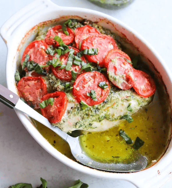 top view of chicken pesto bake in a white oval baking dish topped with tomatoes - Low Carb Chicken Recipes