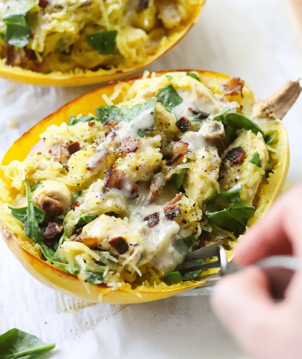 Top view of a spaghetti squash filled with chicken, bacon and cheese.  The chef's hand is holding a fork over the squash