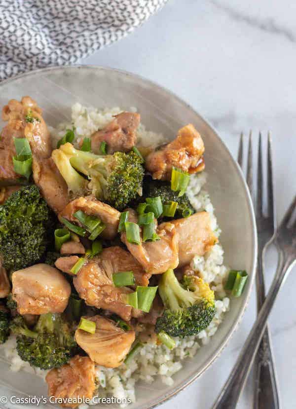 Top view of cooked broccoki and chicken on a grey plate with utensils on the side