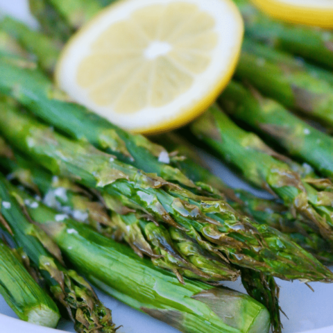 Air fryer asparagus topped with lemon on a white plate.