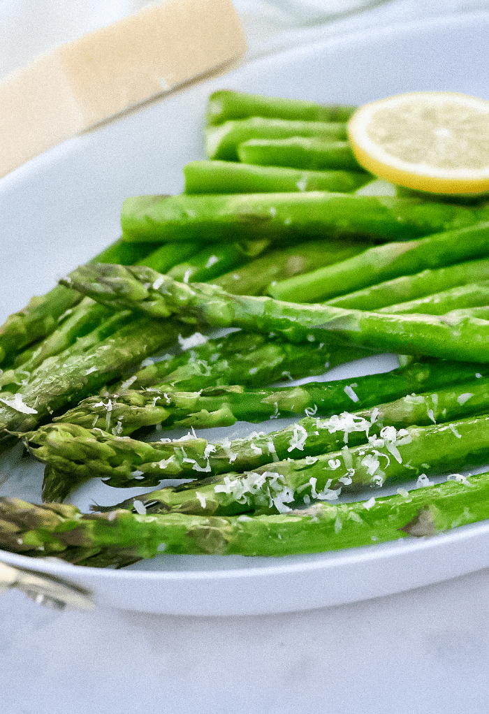 Air fryer asparagus topped with parmesan cheese on a white serving platter. 