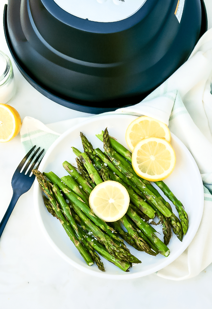 Top view of cooked asparagus on a white serving plate with a fork on the side of the dish. 