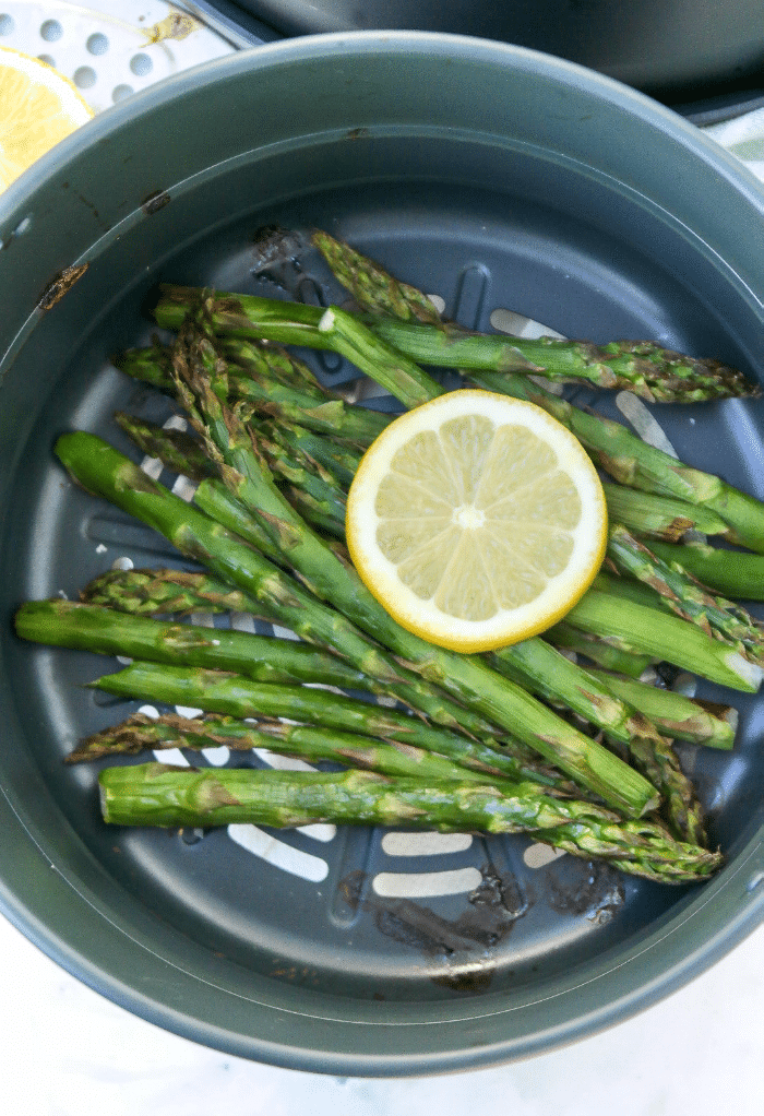 Cooked asparagus in an air fryer topped with a slice of lemon. 