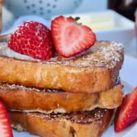 Three slices of Keto French toast topped with fresh strawberries cut in half.