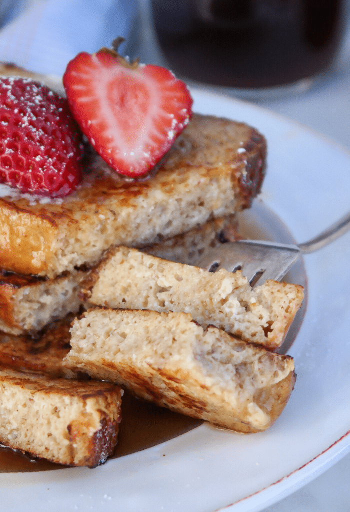 French toast on a white plate with a fork picking up a cut piece. 