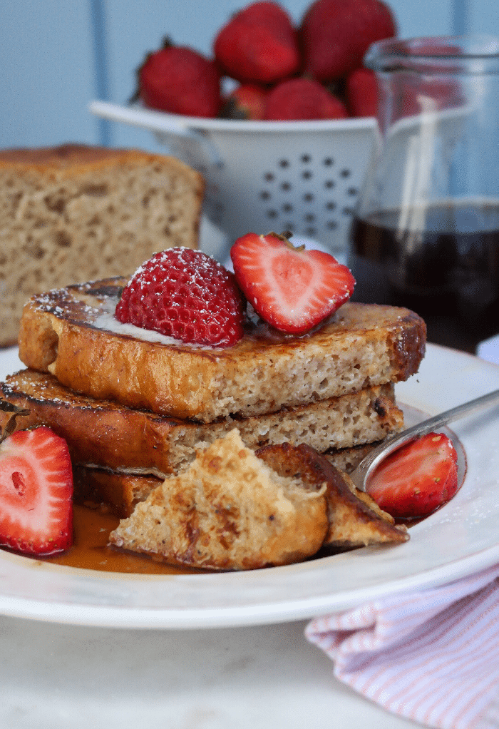 Several slices of Keto French toast on a white plate topped with fresh strawberries. 