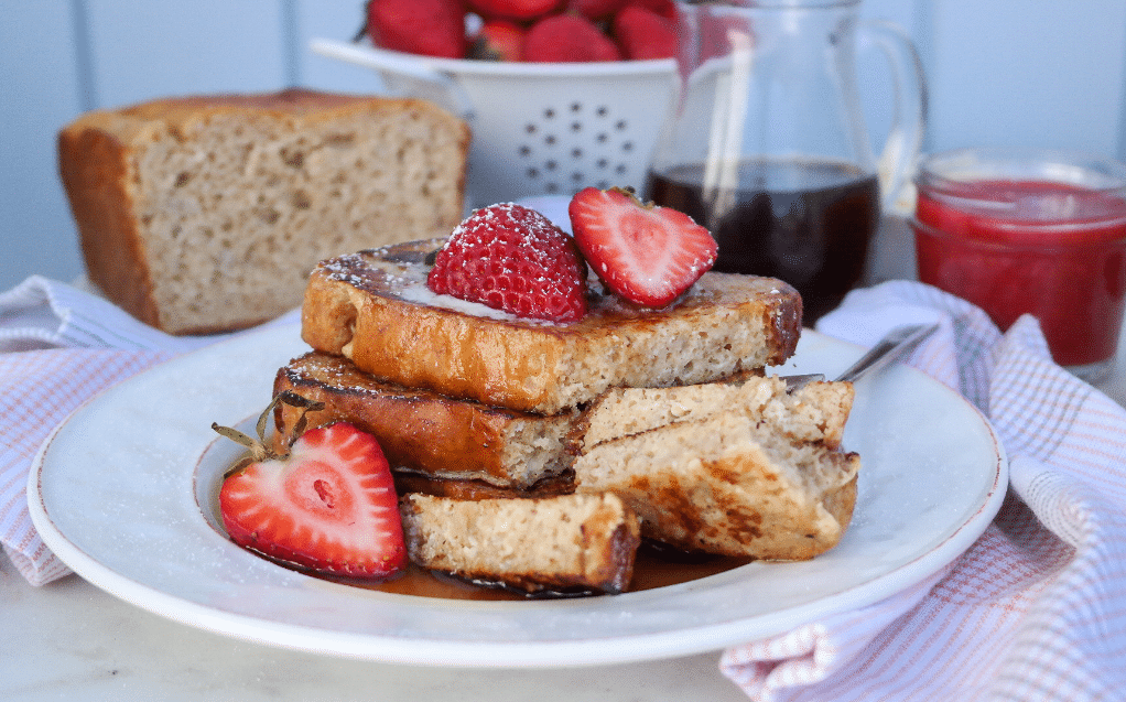 White plate with slices of low carb banana bread topped with strawberries. 