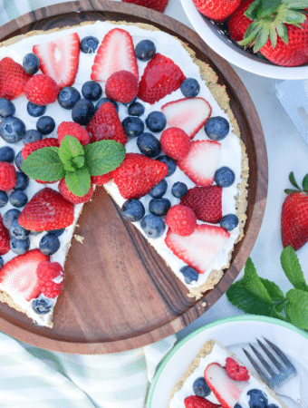 Keto fruit pizza on a wooden serving plate with berries along the side.