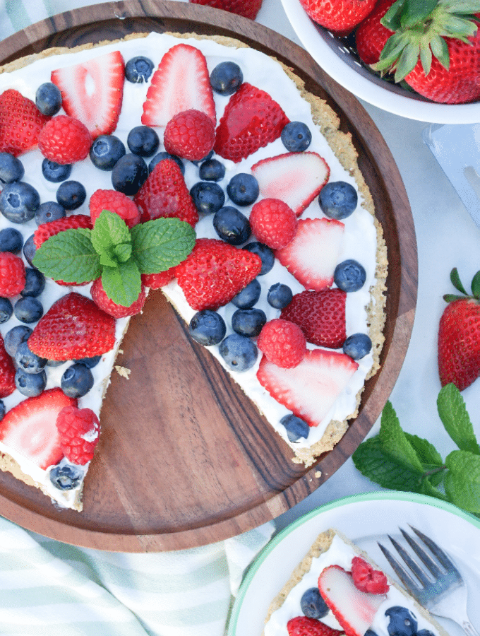 Keto fruit pizza on a wooden serving plate with berries along the side.