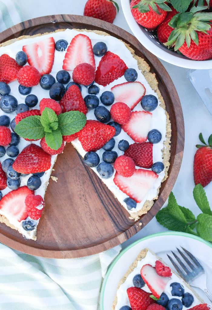 Keto fruit pizza on a wooden serving plate with berries along the side.