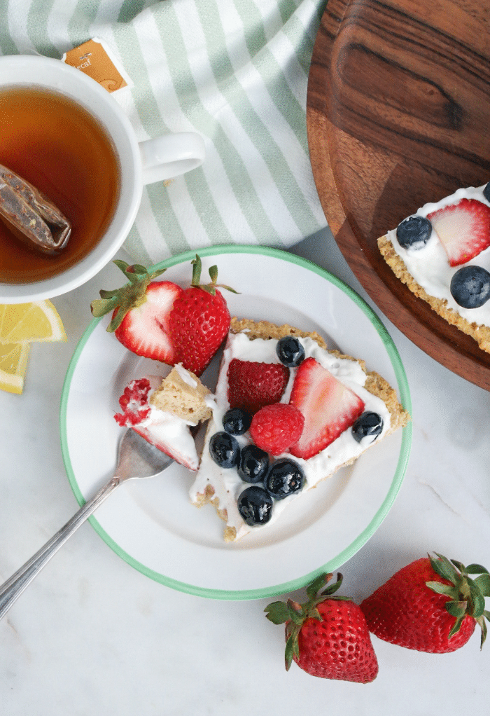 A top view of a piece of keto fruit pizza with tea in a white cup on the side. 