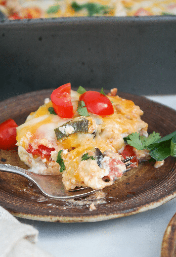 A slice of taco casserole on a brown plate with a fork in front ready to eat. 