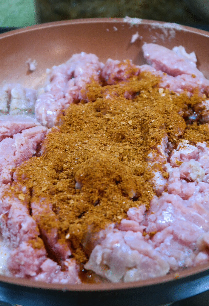 Raw ground turkey with taco seasoning in a large skillet cooking. 