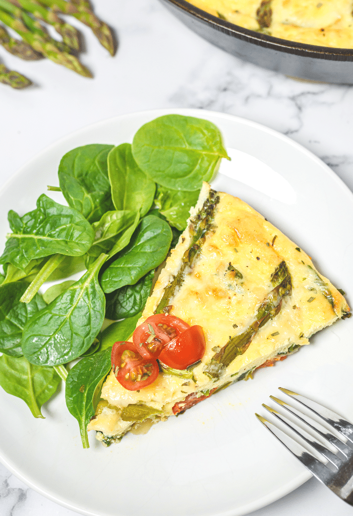 A slice of keto frittata with spinach salad ready to enjoy. 