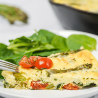Slice of frittata with asparagus on a white plate.