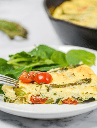 Slice of frittata with asparagus on a white plate.