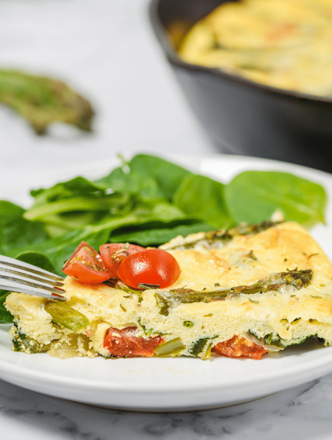 Slice of frittata with asparagus on a white plate.