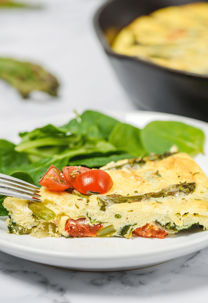 Slice of frittata with asparagus on a white plate. 