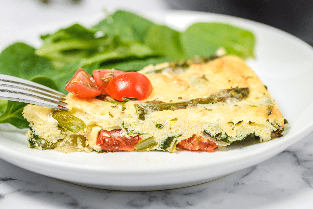 A slice of frittata with asparagus on a white plate. 