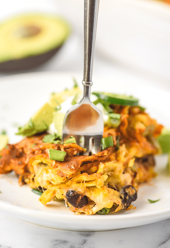 A slice on enchilada casserole with a fork in the middle ready to eat. 