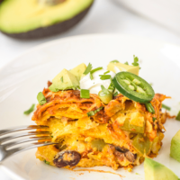 Slice of enchilada casserole topped with a slice of jalapeno and sour cream.