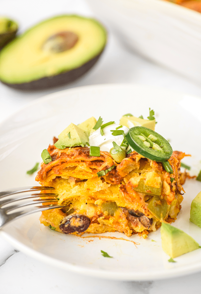 Slice of enchilada casserole topped with a slice of jalapeno and sour cream.