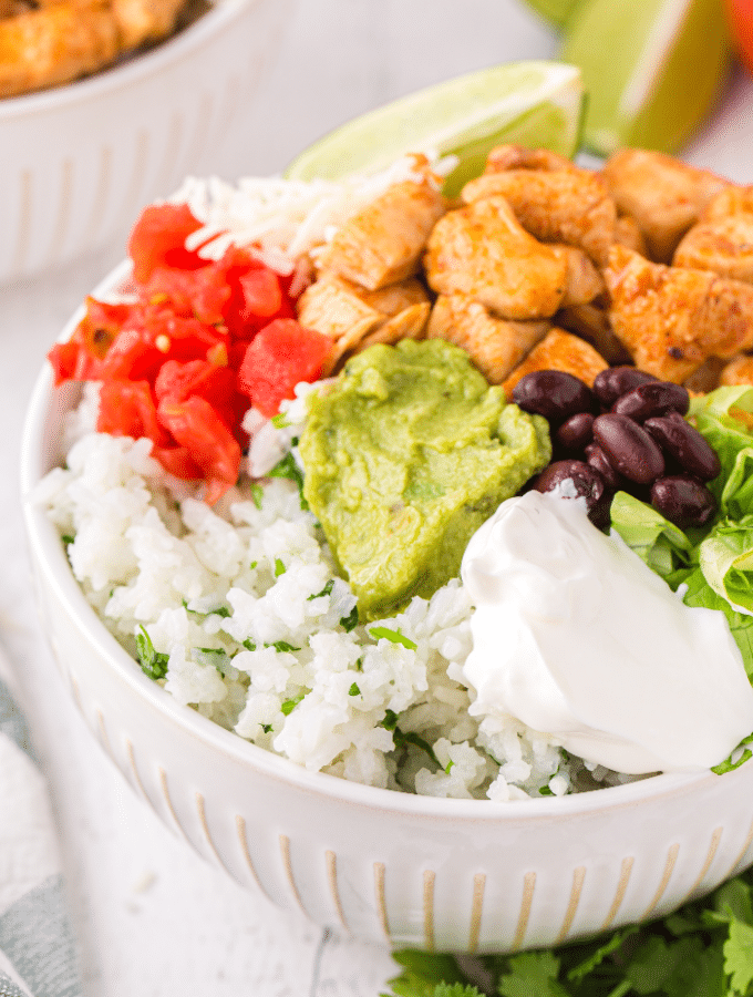 A white bowl with chicken and all the ingredients in a burrito.
