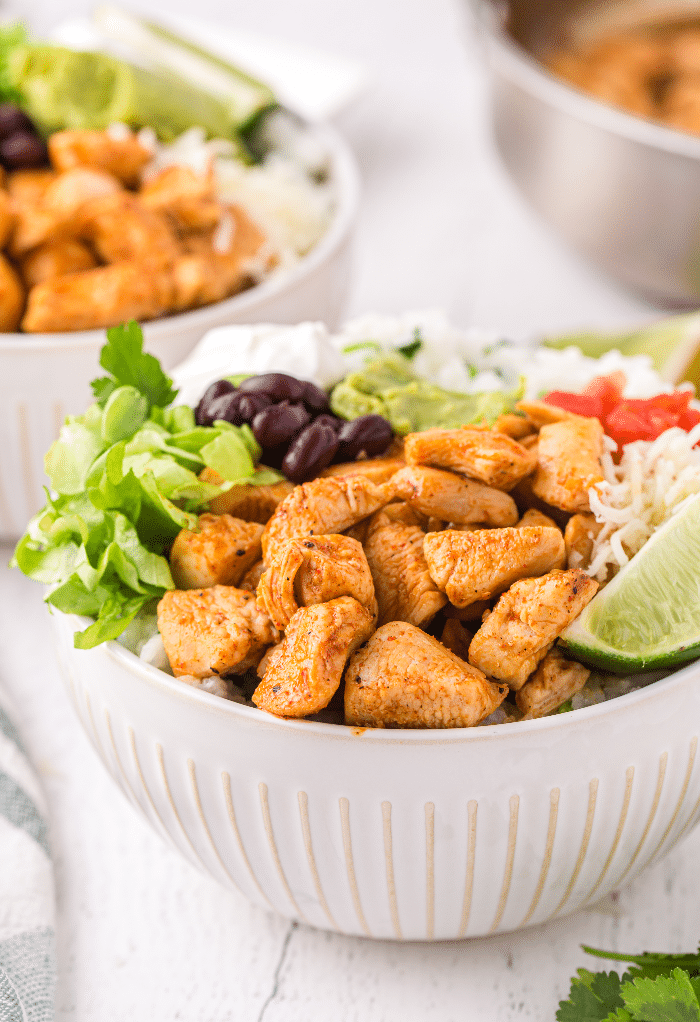 White bowl with chicken and lettuce with lime.