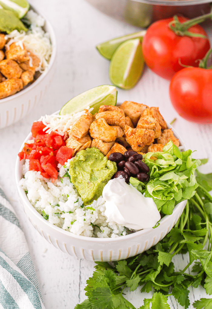 A chicken bowl with tomatoes, beans, rice and guacamole in a white bowl. 