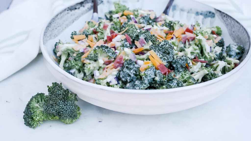 A large ceramic white bowl filled with broccoli salad. 