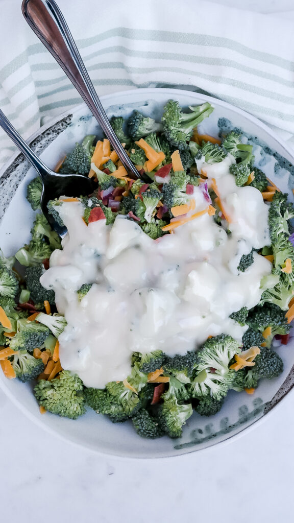 Broccoli salad topped with mayonnaise dressing ready to fold into the salad. 