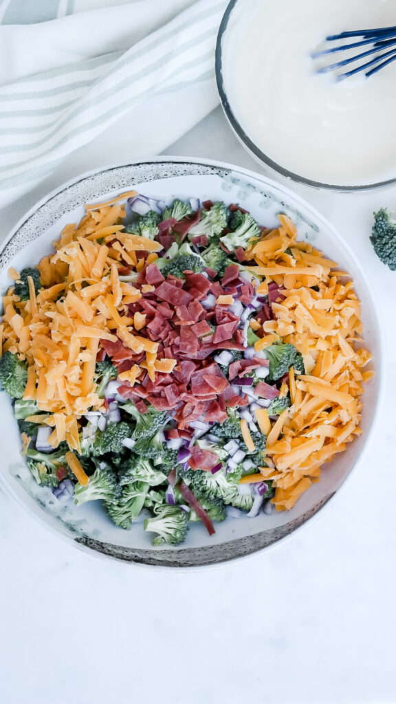 A large white bowl with broccoli, cheese, bacon to make a cold salad. 