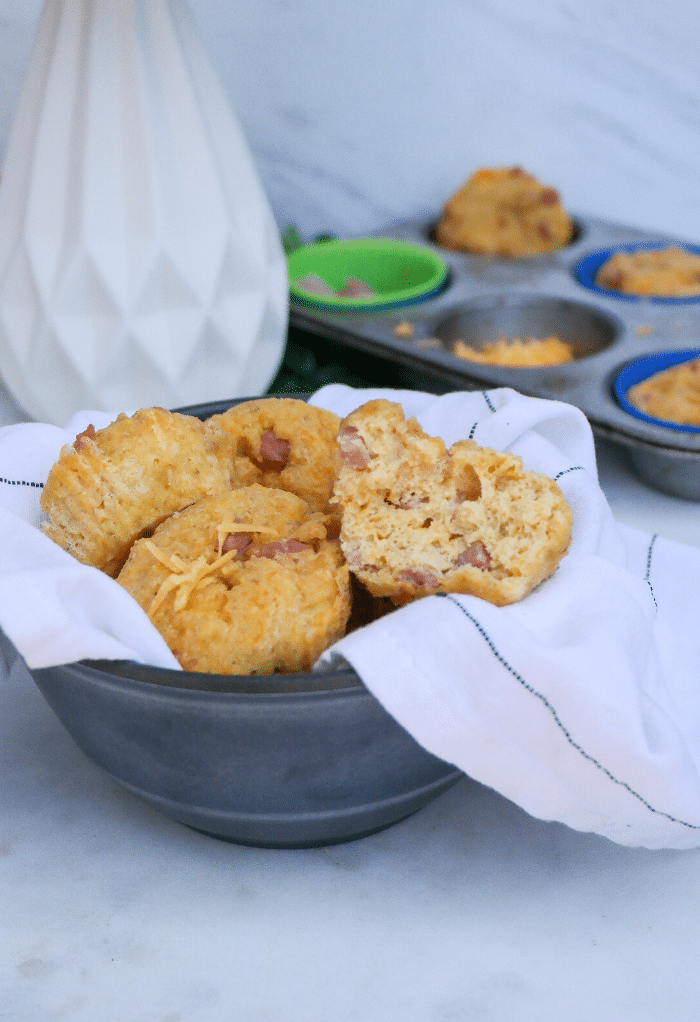 A bowlful of keto muffins with cheese and ham wrapped in a white and blue stripped kitchen towel. 