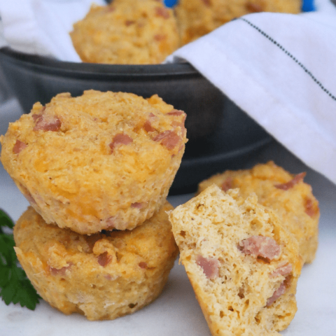 Two savory keto muffins with ham and cheese on top of each other with a half muffin on the side.