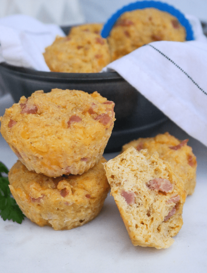 Two savory keto muffins with ham and cheese on top of each other with a half muffin on the side.