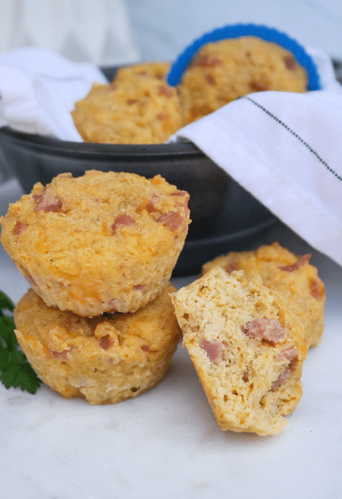 Two savory keto muffins with ham and cheese on top of each other with a half muffin on the side. 
